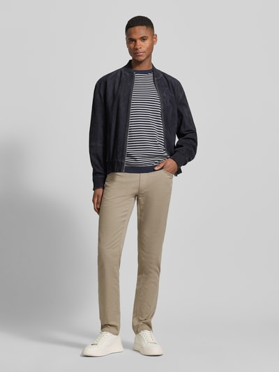 Męski model nosi Slim Fit Hose mit Eingrifftaschen Modell 'Chuck' von Brax, beżowe spodnie z bawełnianego miksu z lyocellem, krój slim fit, kieszenie ukośne, szerokość w rozmiarze 32/32: 43 cm, długość nogawki wewnętrznej: 81 cm, pełen widok z przodu