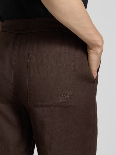 Frauenmodel trägt Leinenhose mit Bindegürtel Modell 'Chiara' von MAC, dunkelbrauner Farbton, sichtbare Struktur, Nahaufnahme Rückansicht, reines Leinen, französische Eingrifftaschen, elastischer Bund.