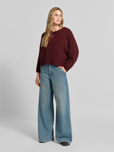 Frauenmodel trägt Oversized Pullover mit Alpaka-Anteil Modell 'East' von American Vintage in Bordeaux, Strick-Optik, Ganzkörperansicht von vorne.