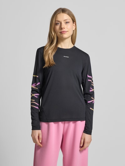 Modelka kobieca nosi czarne Funktionsshirt mit Logo Modell 'Kout' od Salomon, krój regular fit, okrągły dekolt, różowe spodnie, widok całej sylwetki z przodu, długość pleców w rozmiarze S: 58 cm.