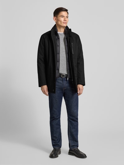 Męski model nosi Regular Fit Jacke mit gefüttertem Stehkragen Modell 'City' od bugatti, czarny kolor, widok całej sylwetki z przodu, długość tyłu w rozmiarze 50: 81 cm, szerokość ramion w rozmiarze 50: 48 cm, szerokość klatki piersiowej w rozmiarze 50: 57 cm, długość rękawa w rozmiarze 50: 65 cm, kieszeń napoleonka, kieszenie boczne na zamek, pełna listwa guzikowa.