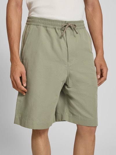 Männermodel trägt Shorts aus Baumwoll-Mix von MAISON KITSUNÉ in hellem Grün, Regular-Fit, elastischer Bund, Eingrifftaschen, Knielänge, Nahaufnahme Oberkörper.