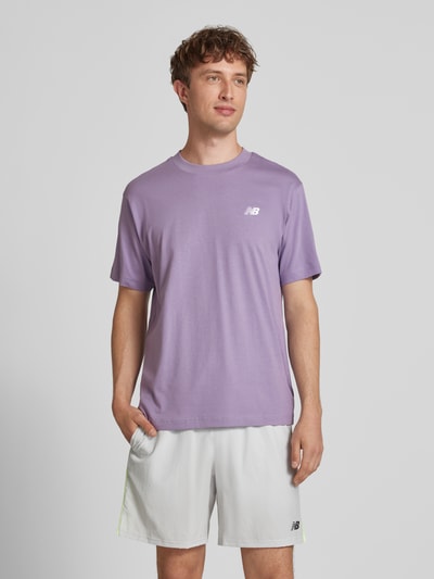 Männermodel trägt T-Shirt mit Logo und Rundhalsausschnitt von New Balance in Lila, Reine Baumwolle, Regular-Fit, Frontansicht, Rückenlänge 74 cm bei Größe M.