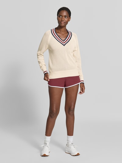 Modelka nosi sweter z dzianiny z dekoltem w serek Model 'maurice' od VARLEY z bawełny, taliowany krój, paski w kontrastowym kolorze, perforowanie, raglanowe rękawy, kremowy z bordowymi detalami, długość tyłu w rozmiarze S: 60 cm, długość rękawów 65 cm, widok całej sylwetki z przodu.