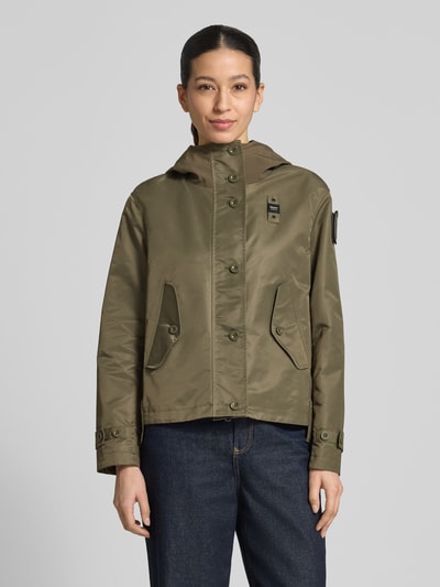 Frauenmodel trägt Damen Jacke von Blauer Usa, Regular-Fit, Logo-Detail, Modell 'Marcela', Kapuze, Eingrifftaschen, olive, Ganzkörperansicht von vorne. Rückenlänge bei Größe S: 60 cm, Schulterbreite: 43 cm, Brustweite: 47 cm, Ärmellänge: 59 cm.