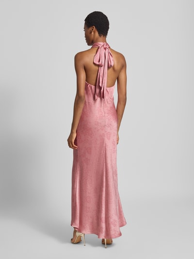 Frauenmodel trägt Abendkleid mit Neckholder Modell 'Fiona' von Neo Noir in Rosa, Satin-Stoff mit floralem Muster, Maxilänge, Ganzkörperansicht Rückansicht. Taillierte Passform, Stehkragen, Rückenlänge bei Größe 36: 139 cm, Brustweite: 38 cm.