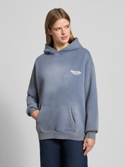 Frauenmodel trägt Oversized hoodie z nadrukiem z logo, efekt znoszenia, mieszanka bawełny, kieszeń kangurka, model 'Wine & Vibe' od ANOTHER COTTON LAB, styl casual, odcień szaroniebieski, gładka faktura, Ganzkörperansicht von vorne.