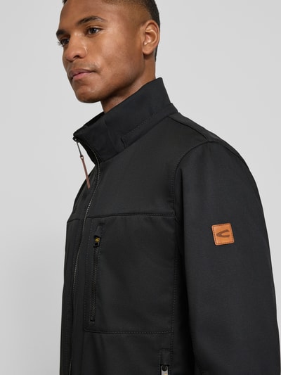 Männermodel trägt Jacke mit Reißverschlusstaschen von camel active in Schwarz, glatte Struktur, Label-Patch, Nahaufnahme Oberkörper.