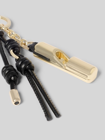 Produktfoto, glänzender goldfarbener Anhänger mit Logo-Detail Modell 'IRIDE' von FURLA, Schlüsselring, Schnapphaken, schwarze Lederbänder, glatte Metall- und Ledertexturen.