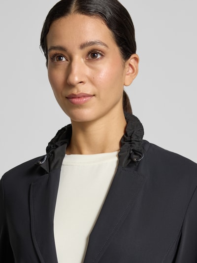 Frauenmodel trägt Slim Fit Blazer mit Stretch-Anteil von Marc Cain, Schwarz, Reverskragen mit Tunnelzug, Nahaufnahme Oberkörper. Elastischer Material-Mix, Knopfleiste, Reißverschlusstaschen, Rückenlänge 25 cm, Brustweite 43 cm, Ärmellänge 63 cm.