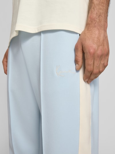 Männermodel trägt Straight Fit Sweatpants mit Logo-Stitching von KARL KANI in Hellblau, Elastischer-Material-Mix mit Baumwoll-Anteil, Ziernähte, Nahaufnahme Oberschenkel.