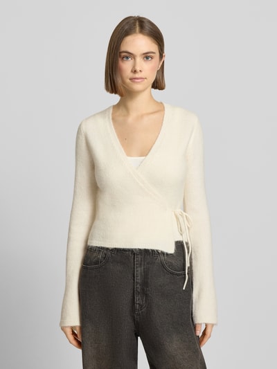 Kobiece modelka nosi Kardigan in Wickel-Optik od Gina Tricot, mieszanka materiałów z domieszką wełny z alpaki, krój slim fit, kopertowy styl, dekolt w serek, długość tyłu 47 cm, długość rękawów 66 cm, kolor kremowy, struktura miękka, widok całej sylwetki z przodu.