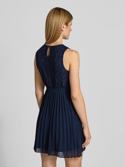 Modelka kobieca nosi Knielanges Kleid mit Spitze od Apricot, mieszanka materiałów z dodatkiem wiskozy, taliowany fason, długość do kolan, koronka, okrągły dekolt, wiązany pasek, spódnica z plisami, wycięcie w kształcie łezki z tyłu, długość tyłu w rozmiarze S: 91 cm, szerokość w rozmiarze S: 39 cm, ciemnoniebieskie odcienie, struktura koronki i gładka, lekka tkanina, widok całej sylwetki z tyłu.