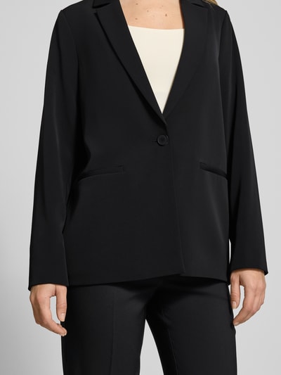 Kobiece model nosi Relaxed Fit Blazer mit Reverskragen od comma, elastyczna mieszanka materiałów, zapięcie na guzik, kieszenie z wypustkami, długość tyłu w rozmiarze 36: 70 cm, szerokość w rozmiarze 36: 49 cm, długość rękawów w rozmiarze 36: 63 cm, kolor czarny, gładka tekstura, całkowity widok z przodu.