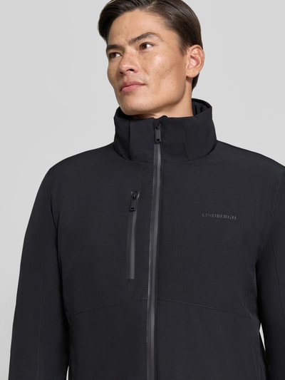 Männermodel trägt Regular Fit Jacke mit Logo-Print von Lindbergh aus elastyczna mieszanka materiałów, czarna, nadruk z logo, napoleońska kieszeń, kaptur z tunelem, Szerokość ramion w rozmiarze M: 46 cm, Szerokość klatki piersiowej w rozmiarze M: 42 cm, Długość tyłu w rozmiarze M: 74 cm, Długość rękawów: 62 cm, Nahaufnahme Oberkörper.