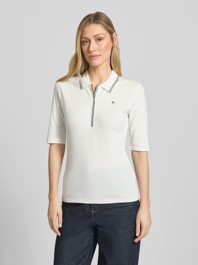 Frauenmodel trägt Slim Fit Poloshirt aus Lyocell-Mix von Tommy Hilfiger, Optik: Unifarben, Logo-Stitching, Kontraststreifen, kurze Knopfleiste, 1/2-Arm, Materialverarbeitung: Piqué, Ganzkörperansicht von vorne.