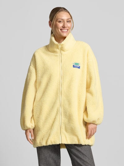 Frauenmodel trägt Oversized Jacke mit Stehkragen Modell 'Hoktown' von American Vintage in hellem Fleece mit Logo-Patch, Ganzkörperansicht von vorne.
