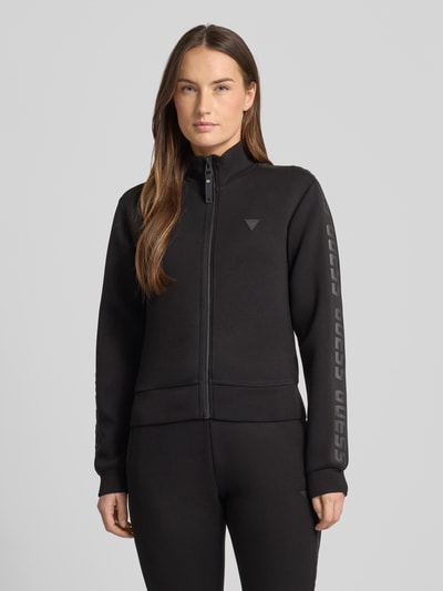 Frauenmodel trägt Regular Fit Sweatjacke aus Viskose-Mix von Guess Activewear in Schwarz mit Logo-Applikation, Ganzkörperansicht von vorne.