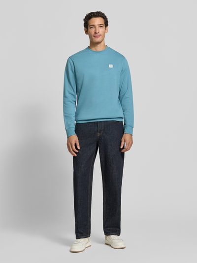 Männermodel trägt Sweatshirt mit Label-Patch von Scotch & Soda aus reiner Baumwolle in Blau, lockerer Schnitt, Ganzkörperansicht von vorne