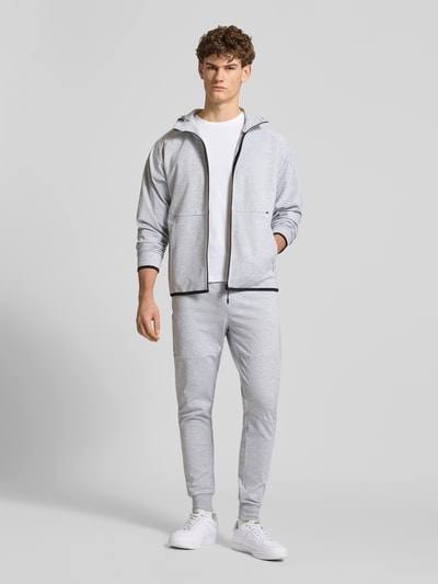 Männermodel trägt lichtgrijze Regular Fit sweatjack met capuchon en ritssluiting, model 'Base' van Jack & Jones, elastische materiaalmix met katoen, steekzakken met ritssluiting, ruglengte bij maat M: 66 cm, mouwlengte bij maat M: 70 cm, volledige voorkantaanzicht