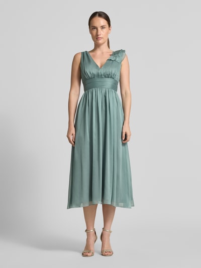 Frauenmodel trägt Cocktailkleid mit V-Ausschnitt von Swing in Grün mit Raffungen, Taillenband und Volants, Ganzkörperansicht von vorne.