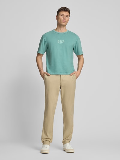 Männermodel trägt T-Shirt mit Logo und Rundhalsausschnitt von GAP in Türkis, Reine Baumwolle, Regular-Fit, Rückenlänge 61 cm, Ganzkörperansicht von vorne.