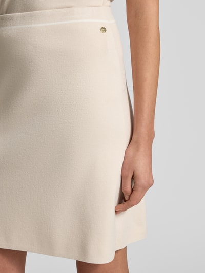 Vrouwenmodel draagt knielange rok uit viscosemix van Marc Cain, lichte A-lijn, logo-detail, crème, detailopname heup en hand.