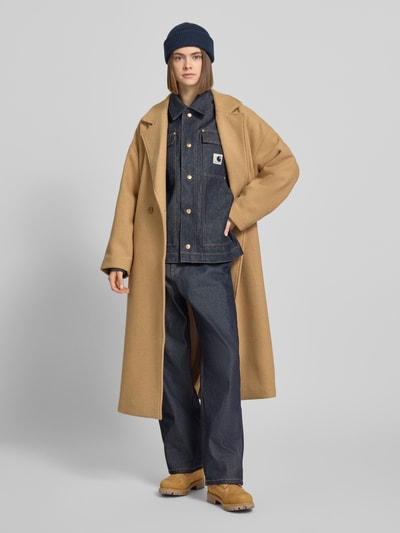 Frauenmodel trägt Regular Fit Jeansjacke mit Logo-Patch Modell 'Arctic' von Carhartt Work In Progress aus reiner Baumwolle in Dunkelblau, Umlegekragen, Brust- und Eingrifftaschen sowie durchgängige Knopfleiste, Ganzkörperansicht von vorne.