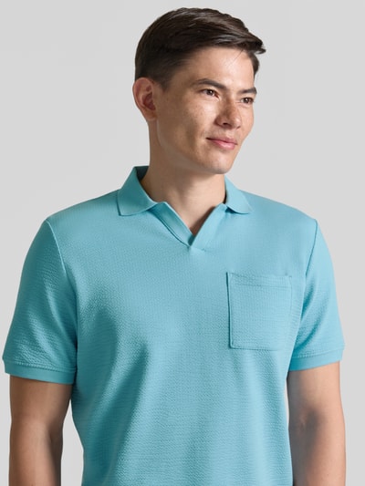 Männermodel trägt Regular Fit Poloshirt aus Baumwoll-Mix von s.Oliver RED LABEL in Hellblau mit Brusttasche, Seersucker-Struktur, Nahaufnahme Oberkörper.