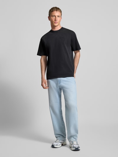 Männermodel trägt Oversized T-Shirt mit Label-Stitching von Pegador aus reiner Baumwolle, schwarzer Farbton, Ganzkörperansicht von vorne.