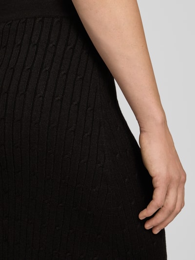 Frauenmodel trägt Strickrock aus Viskose-Mix mit Zopfmuster von Apricot, elastischer Bund, dunkler Stoff, Nahaufnahme Oberkörper.