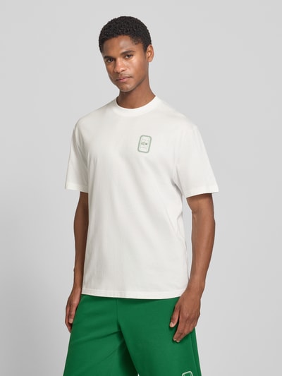 Männermodel trägt Regular Fit T-Shirt aus reiner Baumwolle Modell 'CN Tenniscourt Backprint' von Lacoste in Weiß mit grünem Tennis-Print, Herren T-Shirt, Ganzkörperansicht von vorne.