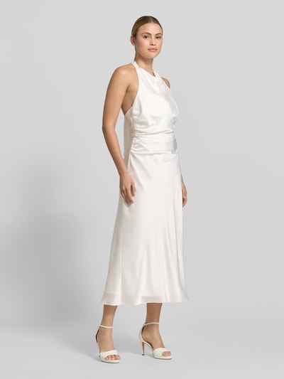 Frauenmodel trägt Slim Fit Midikleid aus Satin von Hey Kyla in Creme mit Raffung, Rückenausschnitt, Neckholder, Ganzkörperansicht von vorne.