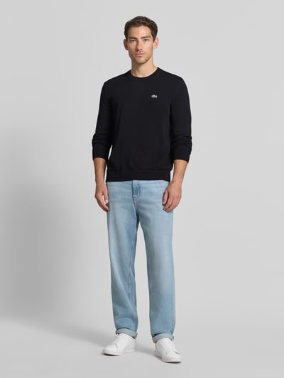 Männermodel trägt Regular Fit Pullover aus Baumwoll-Mix von Lacoste in Dunkelblau, kombiniert mit heller Jeans, Ganzkörperansicht von vorne. Herren Pullover von Lacoste