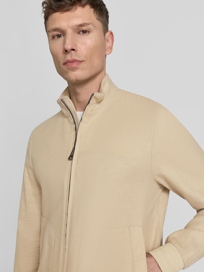 Męski model nosi bluzon z zamek błyskawiczny dwustronny Blouson mit Zweiwege-Reißverschluss od Geox, mieszanka lnu i bawełny, prosty krój, stójka, wpuszczane kieszenie, elastyczne zakończenia rękawów, jasnobeżowy kolor, tekstura gładka, Nahaufnahme górnej części ciała.