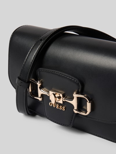 Produktfoto, Handtasche mit Label-Applikation Modell 'JANIE' von Guess, czarny kolor, gładka faktura, metaliczne elementy, Szerokość w rozmiarze 21 cm, długość 13 cm, głębokość 6 cm, długość paska 78 cm, główna komora na magnes, wewnętrzna kieszeń na zamek, regulowany pasek