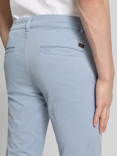 Männermodel trägt Slim Fit Chino aus Baumwoll-Mix von BOSS Orange, Optik: Unifarben, Paspeltaschen, Ganzkörperansicht Rückansicht.