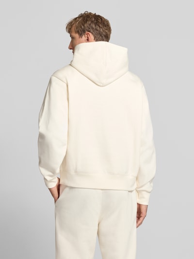 Männermodel trägt Hoodie mit Label-Stitching von Champion aus Baumwoll-Mix, lockerer Schnitt, cremefarben, Ganzkörperansicht Rückansicht.