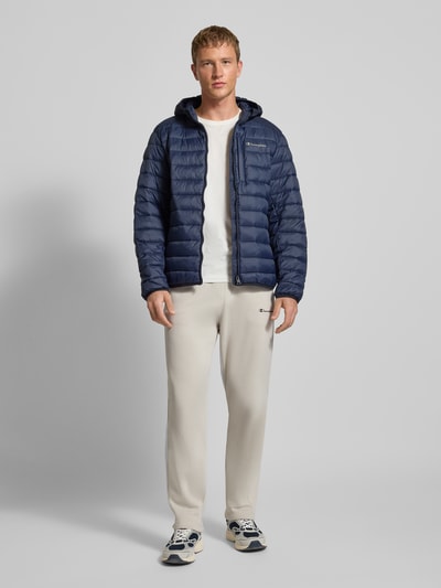 Mannelijk model draagt Steppjacke met Kapuze und Logo van CHAMPION, donkerblauw, rits, insteekzakken, regular fit, voorkant volledige lichaamsweergave.