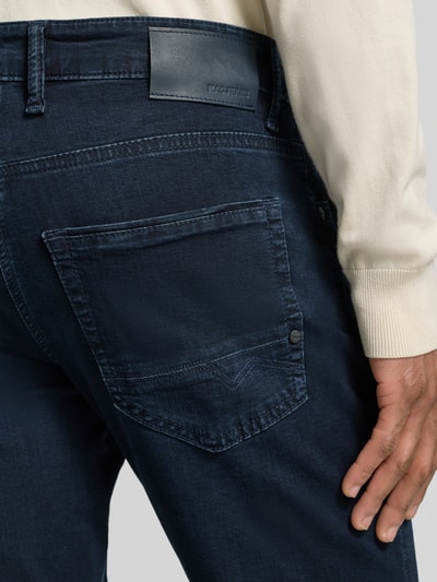 Männermodel trägt Regular Fit Jeans aus Baumwoll-Mix Modell 'Arne Pipe' von MAC in dunkelblau mit 5-Pocket-Design, label-patch, Detailaufnahme Rückansicht.