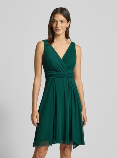 Kobiecy model nosi zielone Cocktailkleid mit V-Ausschnitt von TROYDEN COLLECTION, taliowany krój, podszewka, pas, ujęcie do połowy ciała z przodu.