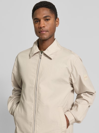Mannenmodel draagt Regular Fit Overshirt uit pure katoen model 'LUTTI' van BOSS Orange in effen beige popeline met label patch, zijzakken, lange mouwen, manchetten, zichtbare ritssluiting, omlegkraag, rugpas met Cacharel-plooi, close-up bovenlichaam vooraanzicht.