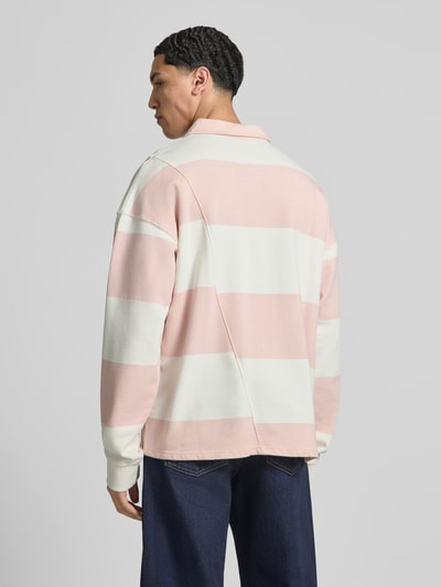Męski model nosi Relaxed Fit Poloshirt aus reiner Baumwolle Modell 'Castelluccio' von Pegador, różowe i białe pasy, wyhaftowane logo, dół zaokrąglony, długość tyłu w rozmiarze M: 69 cm, krój relaxed fit, kołnierzyk polo z listwą guzikową, ściągacze na rękawach, luźne ramiona, Ganzkörperansicht Rückansicht.