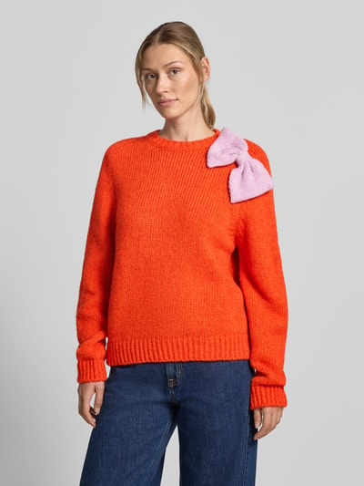 Frauenmodel trägt Relaxed Fit Pullover aus Baumwoll-Mix Modell 'KOLLIER' von Essentiel Antwerp, leuchtend orange mit rosa Strickschleife, Kombination aus weicher Struktur und kräftigen Farben, Nahaufnahme Oberkörper, Damen Pullover von Essentiel Antwerp.