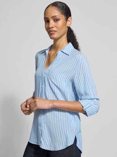 Frauenmodel trägt Comfort Fit Hemdbluse aus reiner Viskose von s.Oliver RED LABEL mit blau-weißem Allover-Streifenmuster, Hemdblusenkragen, Brusttasche und abgerundetem Saum, Ganzkörperansicht von vorne.