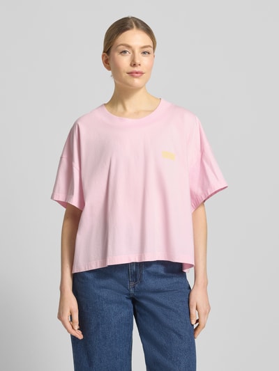 Frauenmodel trägt T-Shirt mit überschnittenen Schultern Modell 'GIXY' von American Vintage in Rosa, Reine Baumwolle, Logo-Print, Lockerer-Schnitt, Rundhalsausschnitt, Rückenlänge bei Größe XS/S 47 cm, Ganzkörperansicht von vorne.