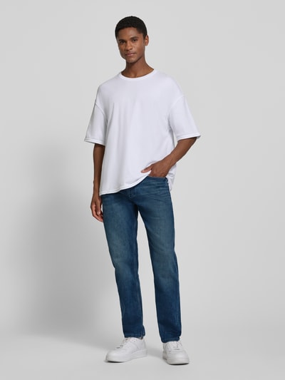Männermodel trägt Tapered Fit Jeans aus Baumwoll-Mix von s.Oliver RED LABEL in mittelblauer Waschung, Ganzkörperansicht von vorne.