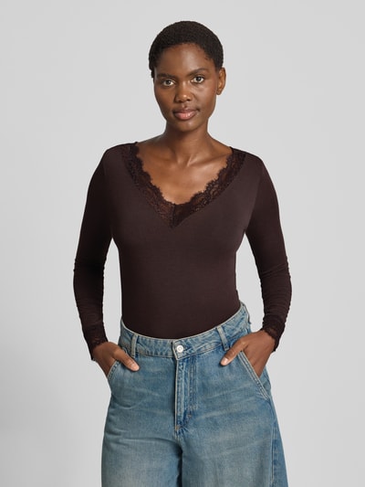 Kobiece model nosi bluzkę z długim rękawem Slim Fit Langarmshirt aus Modal-Mix mit Woll-Anteil Modell 'SKYE' od VERO MODA w kolorze ciemnobrązowym, gładka struktura, koronka przy dekolcie, szerokie niebieskie jeansy, widok całej sylwetki z przodu.