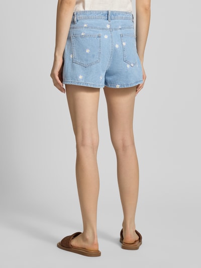 Frauenmodel trägt Regular Fit Skort aus reiner Baumwolle Modell 'LESLY' von Only in hellblauem Denim mit Stickerei, Gesäßtaschen, Ganzkörperansicht Rückansicht.