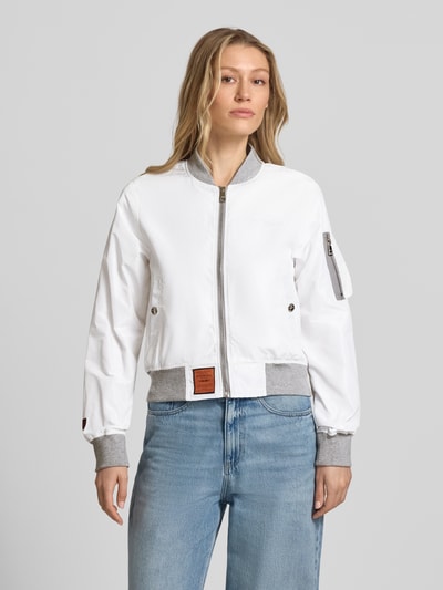Frauenmodel trägt Bomberjacke mit Label-Patch und Reißverschlusstasche am Ärmel von Original Bombers in Weiß mit Stehkragen, silbergrauen elastischen Abschlüssen, Logo-Stitching und seitlichen Eingrifftaschen mit Druckknopfverschluss, lockerer Schnitt, Obermaterial glatte Textur, Jeans, Ganzkörperansicht von vorne. Rückenlänge 53 cm, Schulterbreite 37 cm, Brustweite 48 cm, Ärmellänge 63 cm, Größe S.